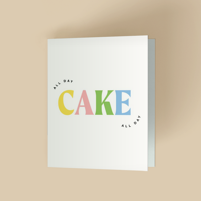 Birthday or celebration card with white background. The word "CAKE" is in large, bold, multicolor serif letters - yellow C, pink A, green K, blue E- centered. Small black sans-serif text "ALL DAY" arched above the C and below the E.