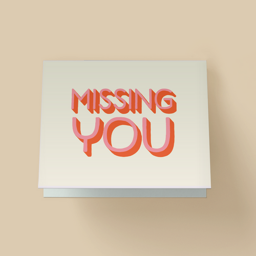 White greeting card. The words "MISSING YOU" are in large, retro-style #D block letters - light pink font face with burnt orange shadow/extrusion - stacked in two lines and centered.