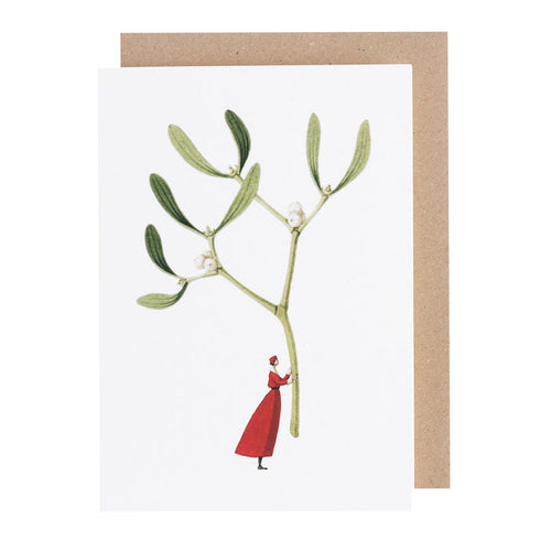 A white greeting card featuring a whimsical illustration of a small woman in a red dress holding up a gigantic sprig of mistletoe by the stem. Kraft paper envelope included.