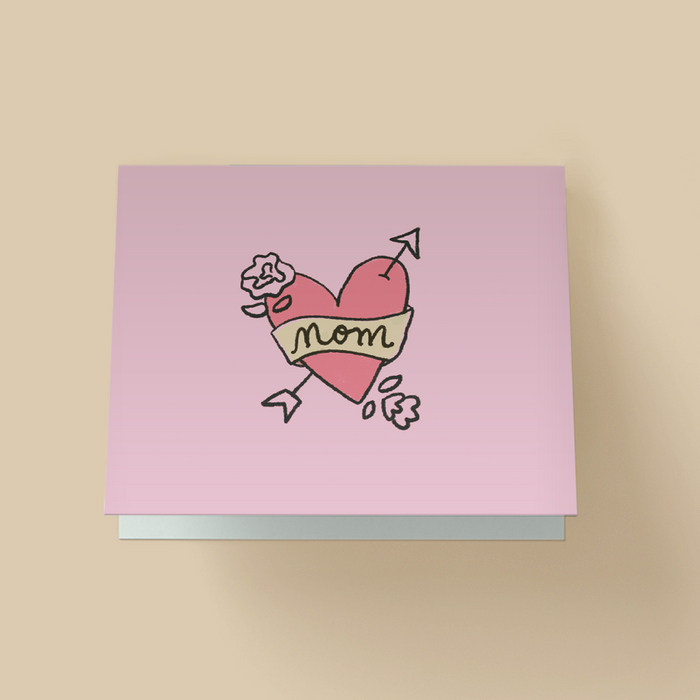 Mother's Day greeting card with hand-drawn tattoo-style illustration. A pink heart is pierced by an arrow, wrapped with a light yellow banner that says "Mom" in script, with small flowers and petals around it. Background is pale pink