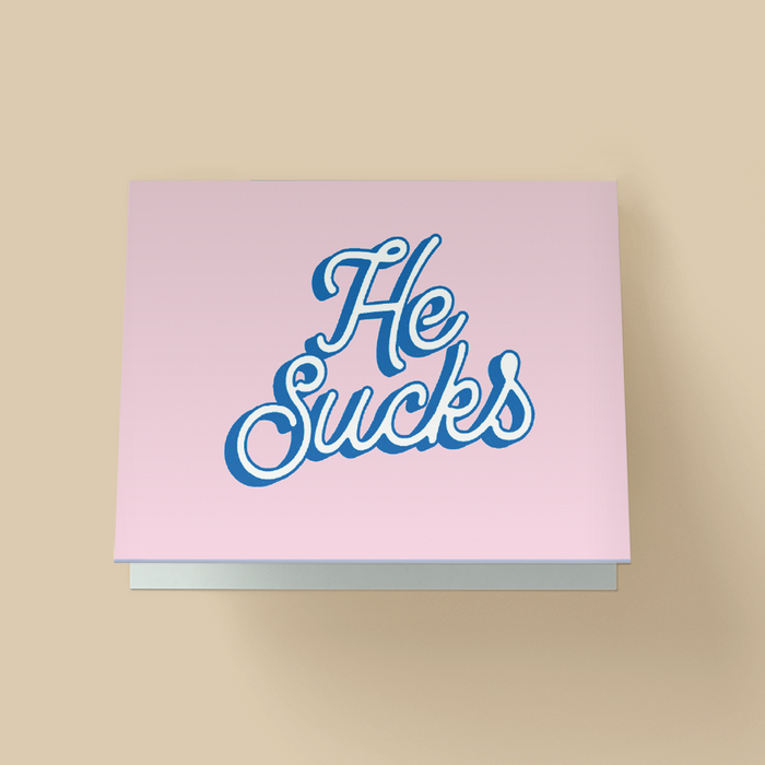 Greeting card with a light lavender-pink background. The text "He Sucks" is in large, white, retro cursive script with a blue drop shadow, stacked diagonally in the center.