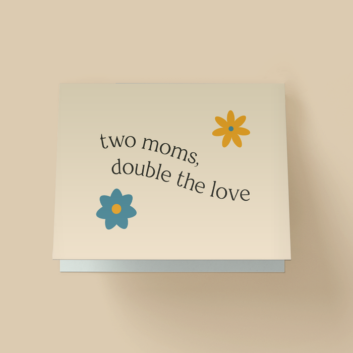 Minimalist  Mother's Day card with off-white background. Black serif text in the center reads 'two moms, double the love' in a curved, arched layout. Two flat illustrated flowers - an orange flower with a blue center in the top right, and a blue flower with an orange center in the bottom left.