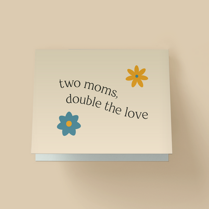 Minimalist  Mother's Day card with off-white background. Black serif text in the center reads 'two moms, double the love' in a curved, arched layout. Two flat illustrated flowers - an orange flower with a blue center in the top right, and a blue flower with an orange center in the bottom left.